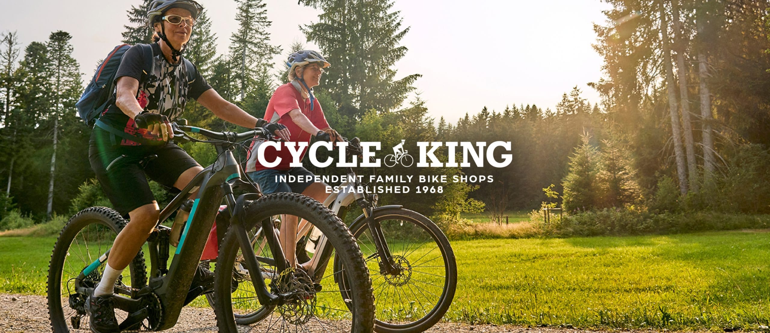 Two women riding bikes in a forest setting. Cycle Kings logo sits on top of the image